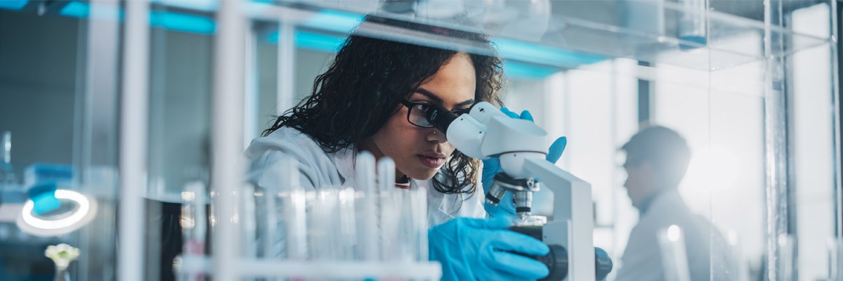 Healthcare lab worker analyzes specimen under microscope